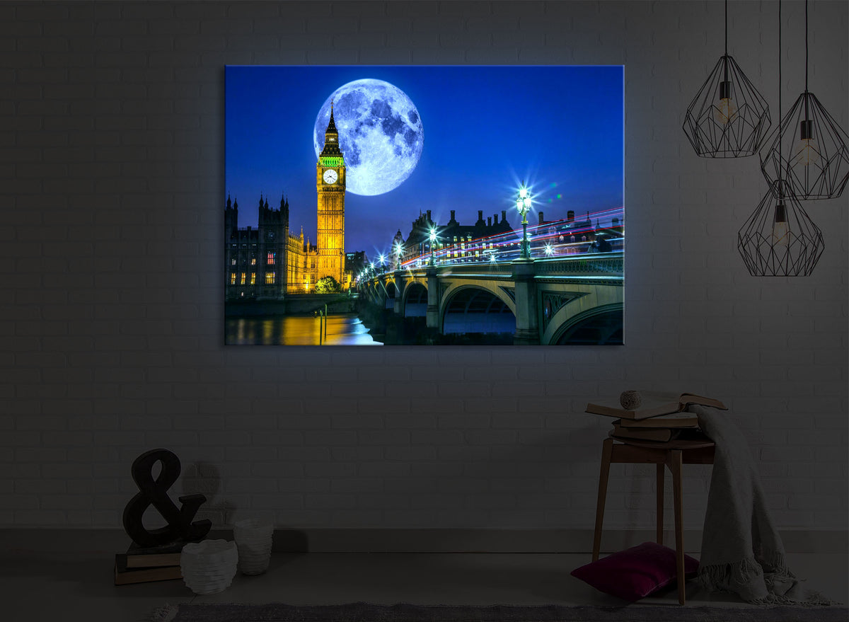 beleuchtetes bild mit dem Motiv Big Ben vor großen Mond in London in einem dunklen Raum. Das Bild leuchtet blau im abgedunkelten Zimmer