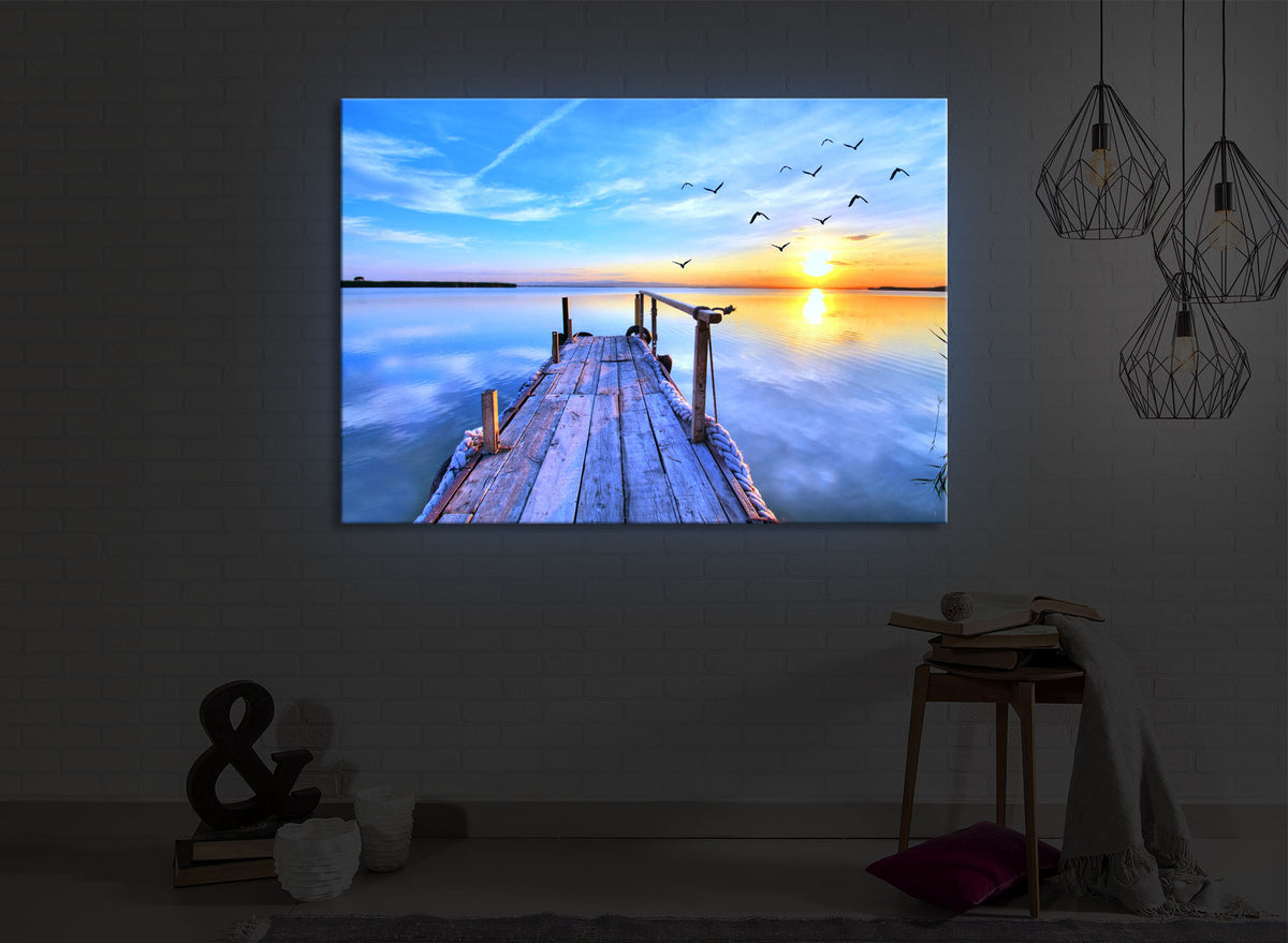 beleuchtetes bild mit dem Motiv Steg mit Möwen bei Sonnenuntergang in einem dunklen Raum. Das Bild leuchtet blau im abgedunkelten Zimmer