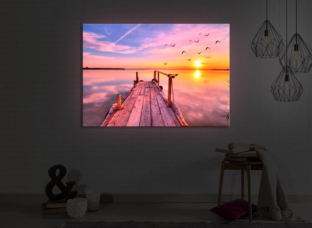 leuchtbild mit dem Motiv Steg mit Möwen bei Sonnenuntergang in einem dunklen Raum. Das Bild leuchtet rot im abgedunkelten Zimmer
