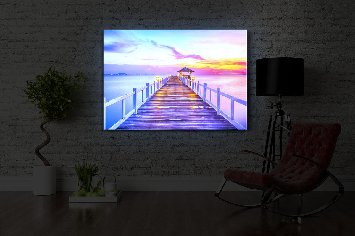 beleuchtetes bild mit dem Motiv Steg ins Meer bei Sonnenuntergang in einem dunklen Raum. Das Bild leuchtet blau im abgedunkelten Zimmer