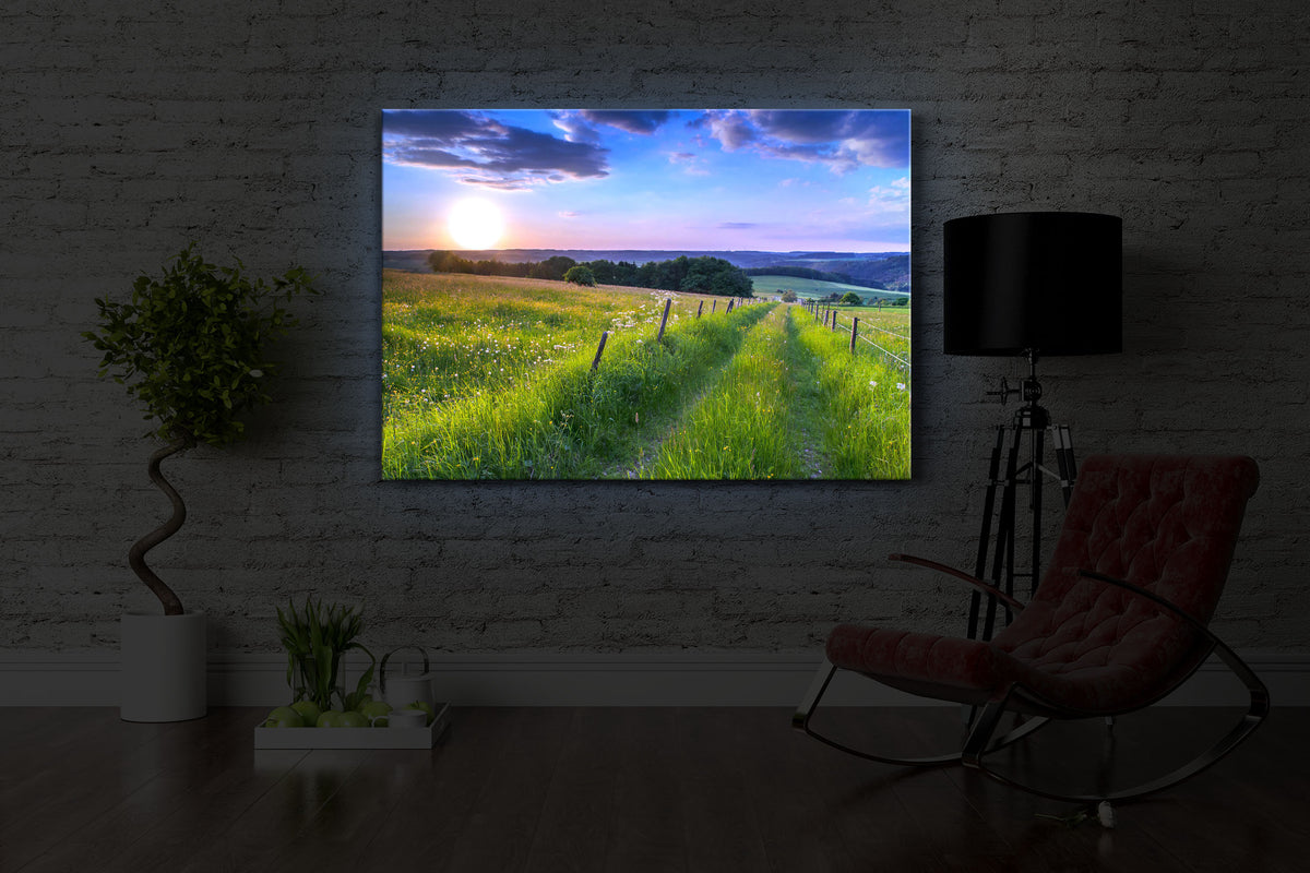 beleuchtetes bild mit dem Motiv Wunderschöne Bergwiese im Sonnenaufgang in einem dunklen Raum. Das Bild leuchtet blau im abgedunkelten Zimmer